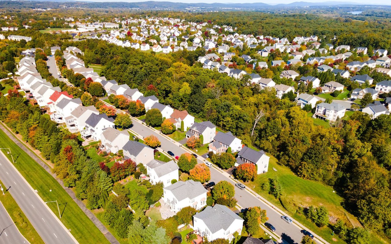 Aerial view of a suburban neighborhood with detached homes, dense trees, and autumn foliage.