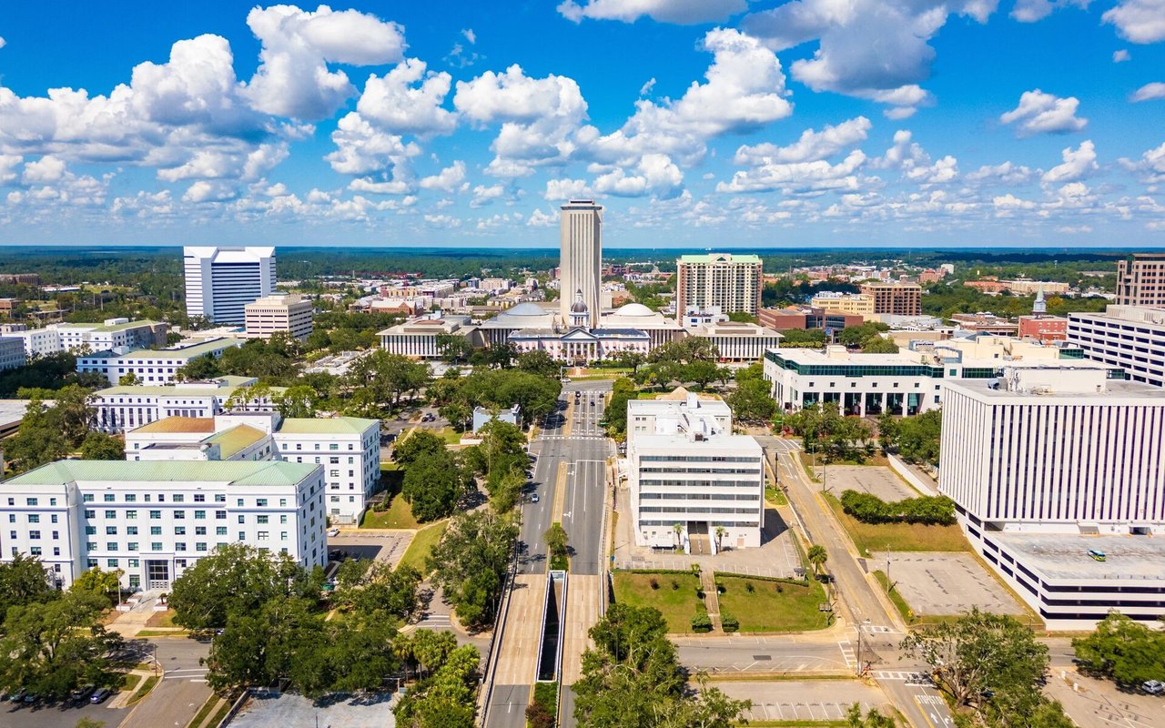 Aerial view of downtown Tallahassee, with the Capitol complex and city skyline under a bright, cloud-filled sky.