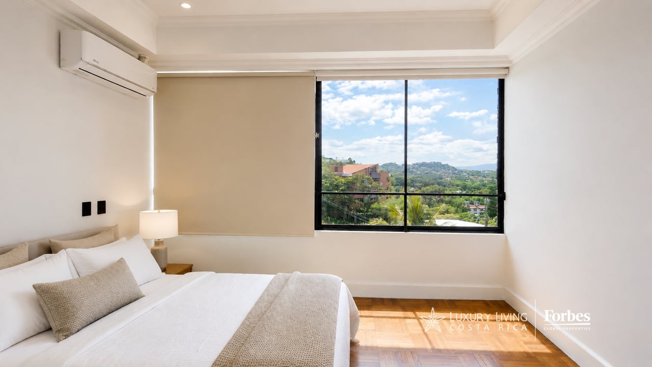 Furnished bedroom with a white bed and a large window overlooking green hills.