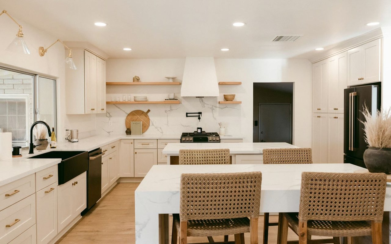 Bright white kitchen with a marble-look island, open wood shelves, and woven bar stools.