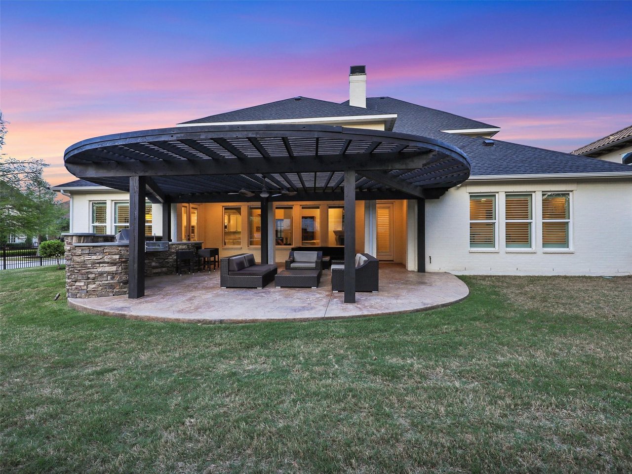 Luxury outdoor living patio with pergola and outdoor kitchen at sunset in Newman Village, Frisco TX — showcasing the indoor-outdoor lifestyle of North DFW luxury homes.