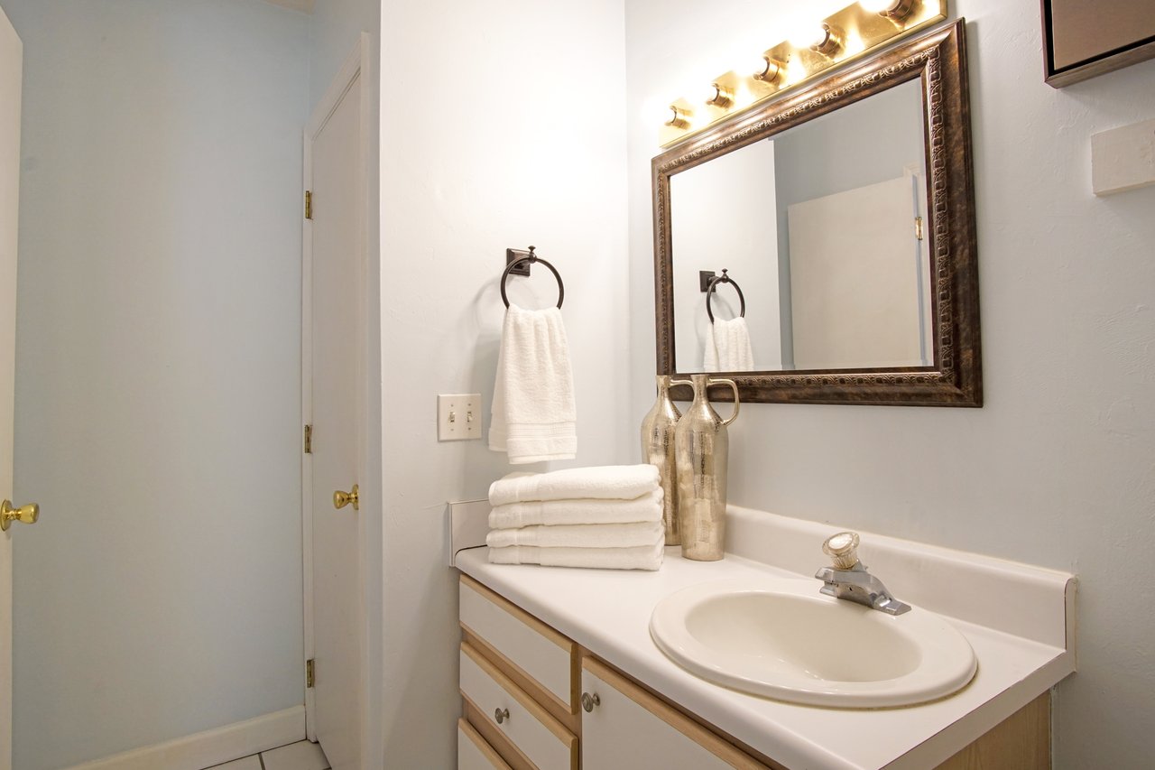 Bright bathroom with light blue walls, a large framed mirror, and white sink. Towels are neatly folded beside metallic vases, creating a tidy, serene atmosphere.Bright bathroom with light blue walls, a large framed mirror, and white sink. Towels are neatly folded beside metallic vases, creating a tidy, serene atmosphere.