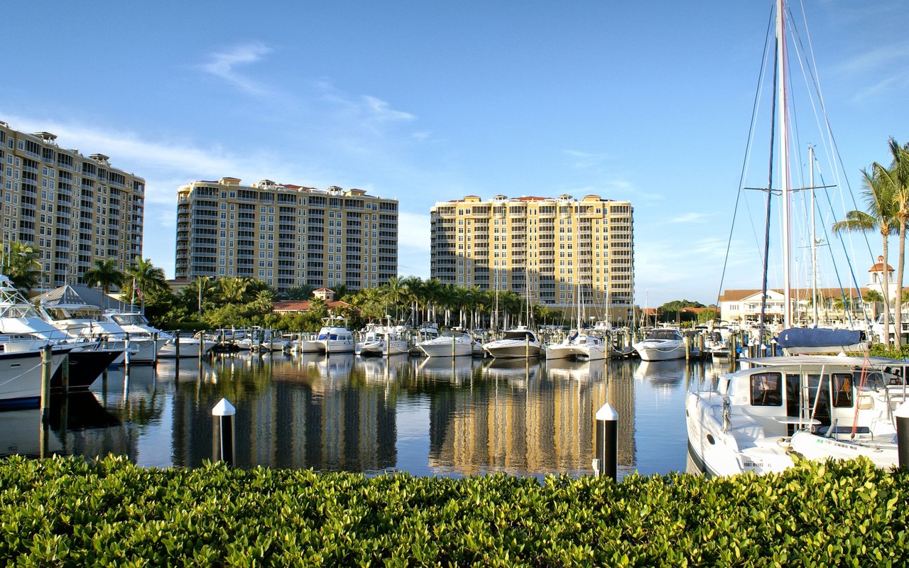 West Marina harbor with moored boats, sailboat masts, and waterfront condominium towers.