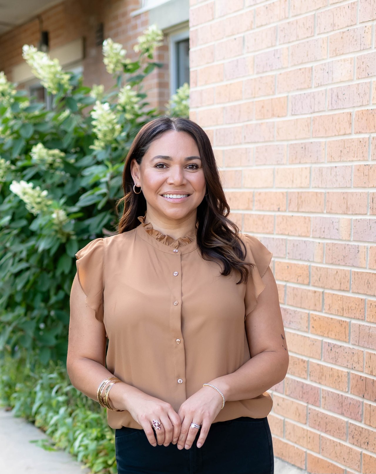 Britt Munoz standing beside a brick wall, wearing a tan blouse.
