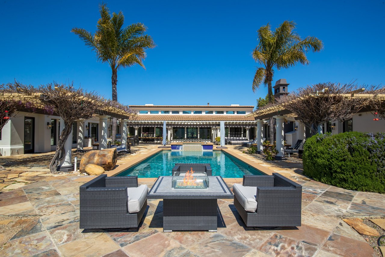 Courtyard pool with a raised spa, patio seating, and a fire table framed by palm trees.