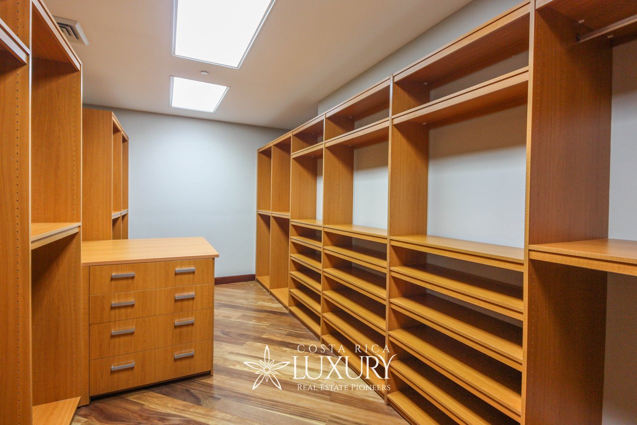 Walk-in closet with extensive built-in wooden shelving and a central drawer unit.