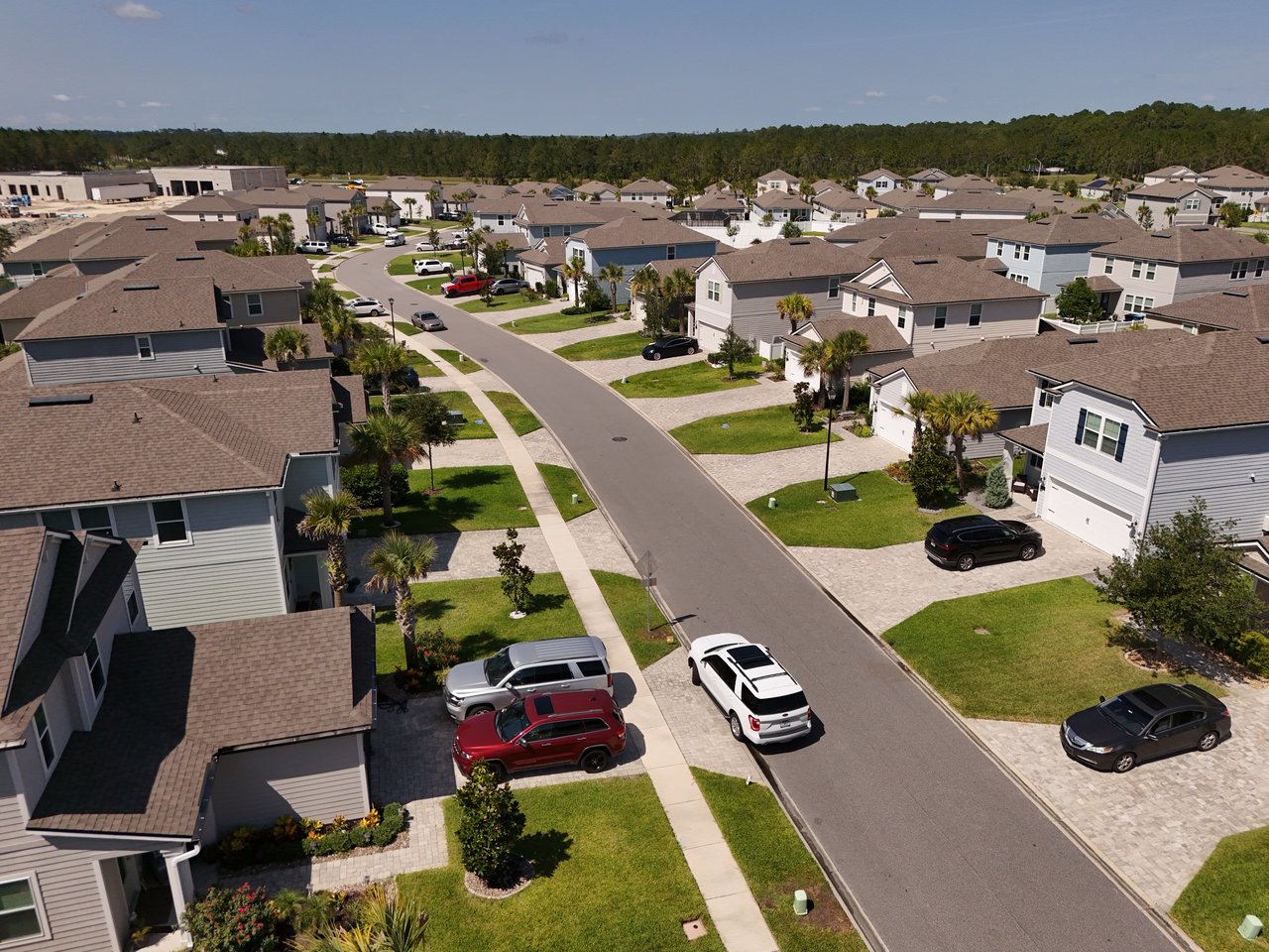 Aerial view of a residential neighborhood with rows of homes along a curving street and palm-lined lawns.