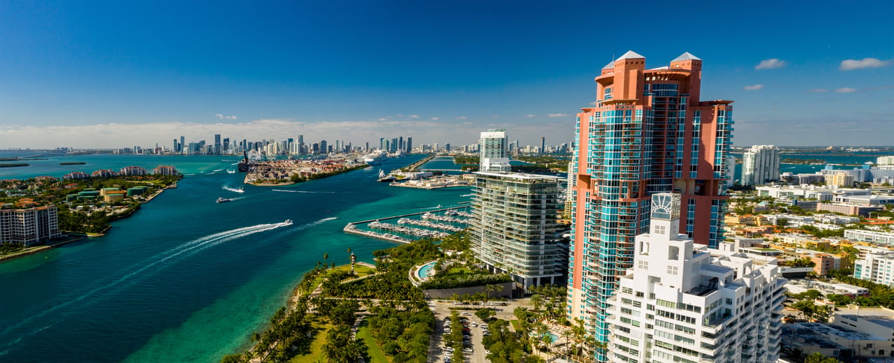 Miami waterfront with a red-and-glass condominium tower overlooking Biscayne Bay and the downtown skyline.