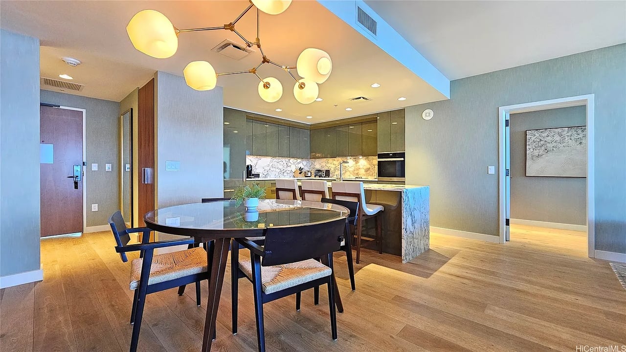 Open-plan kitchen and dining area with a glass table, marble island, and globe pendant lights.