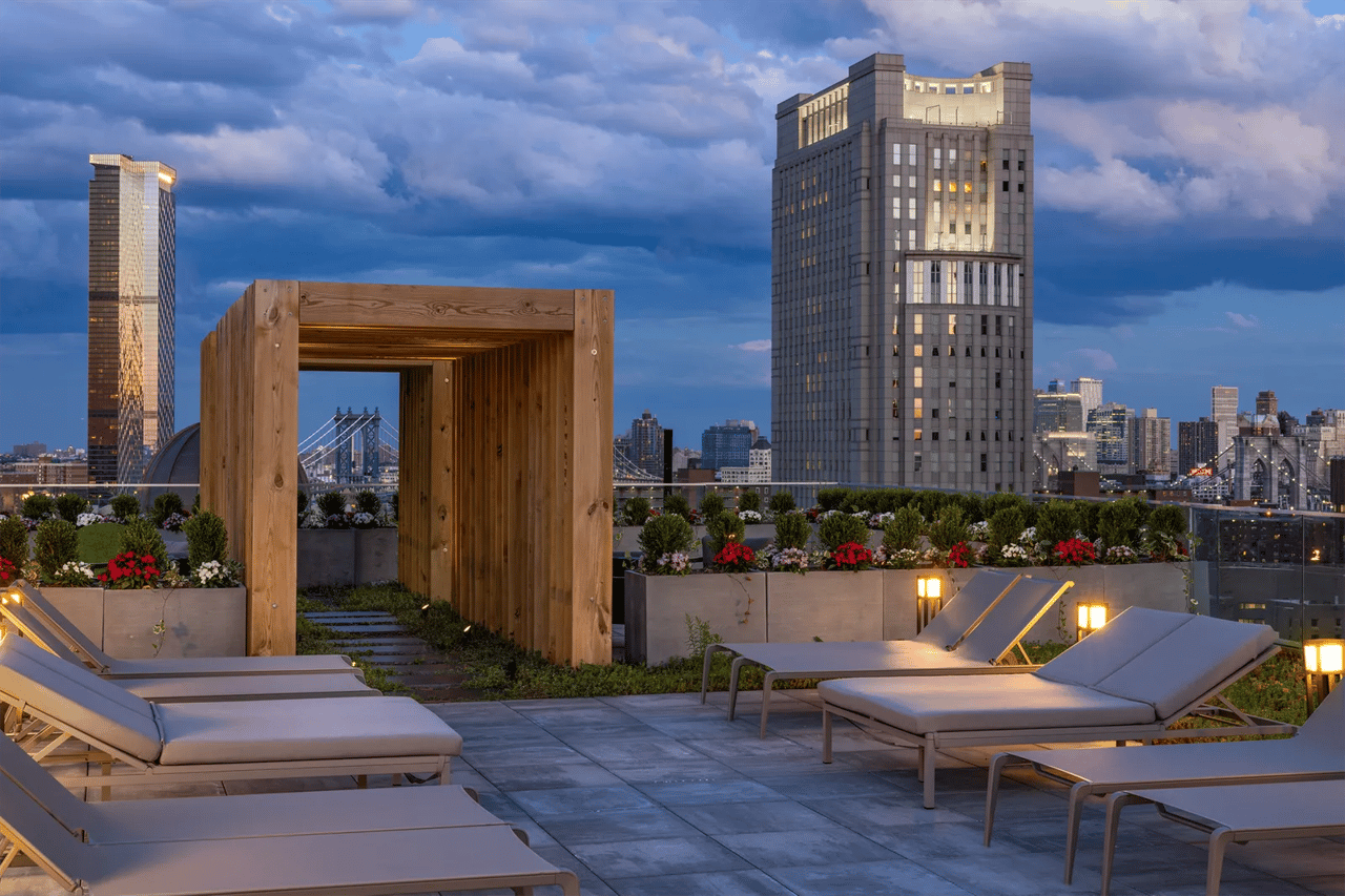 108 Leonard rooftop terrace with lounge chairs, a wooden pergola, and Manhattan skyline views at dusk.