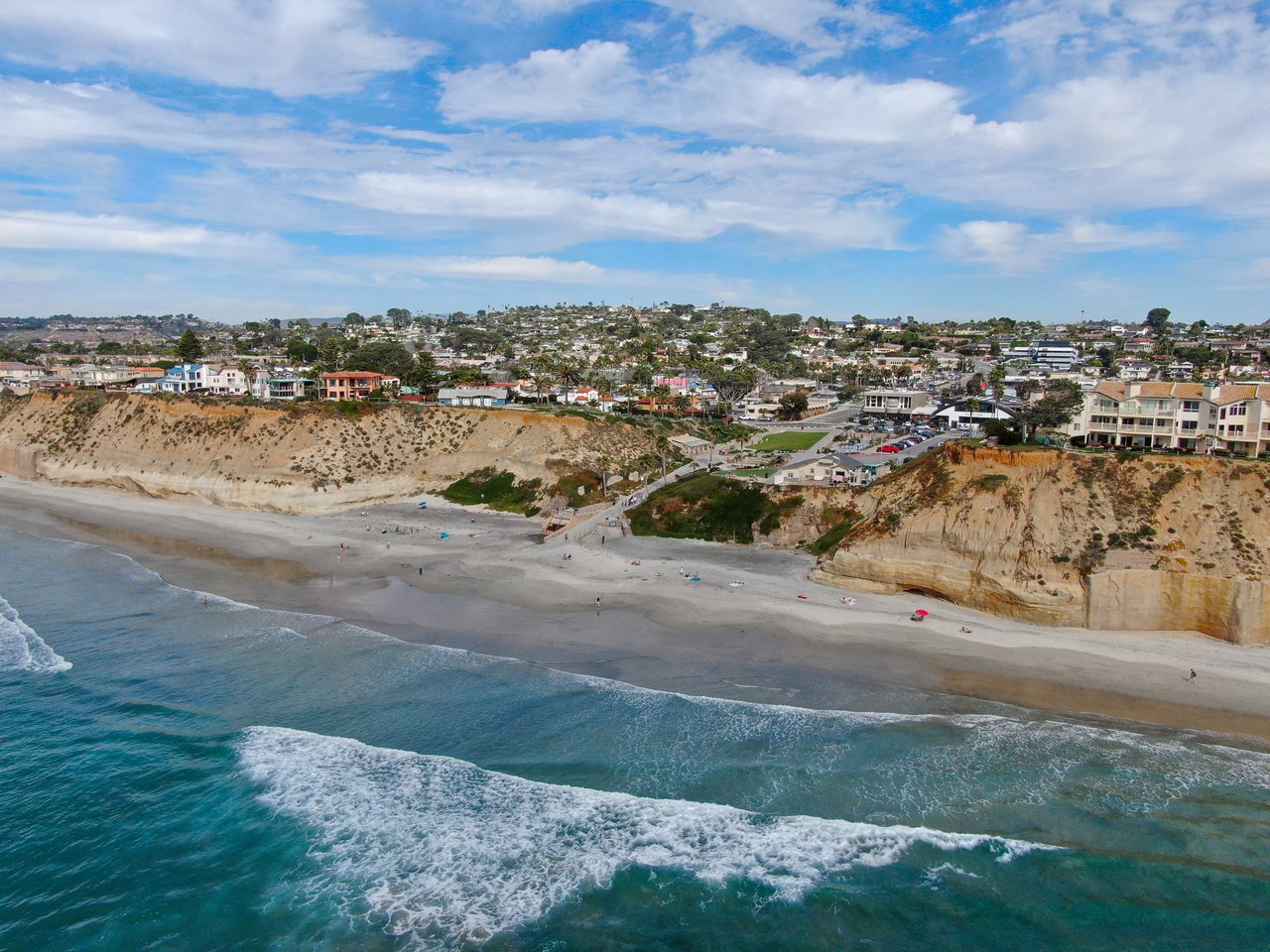 Coastal neighborhood above a sandy beach, with ocean waves and homes along the bluffs.