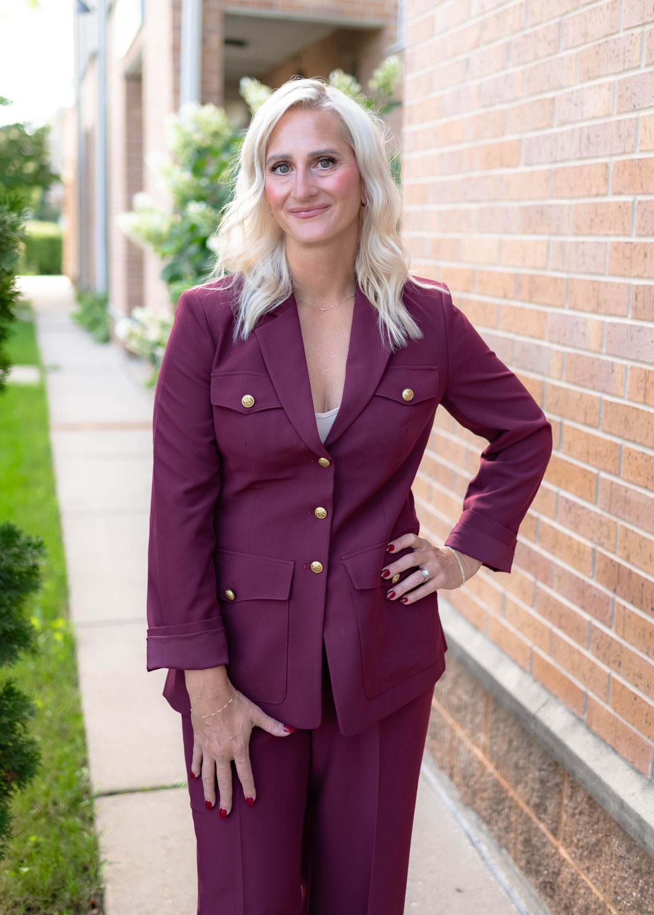 Bailey Nye stands beside a brick building in a plum suit.