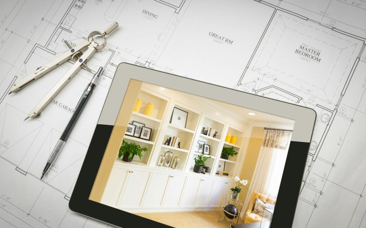  A blueprint of a house plan is laid out on a light-colored surface, with a silver drafting compass and a pen placed on it.