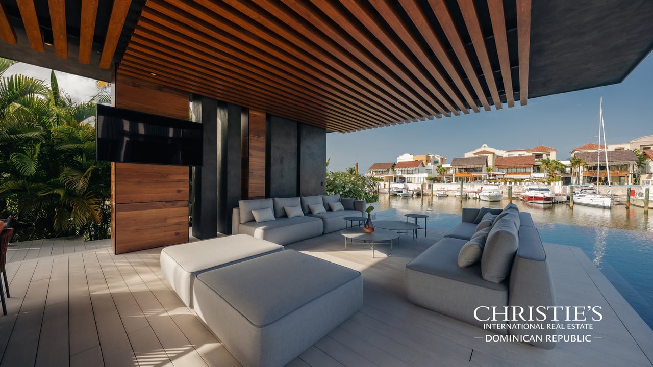Covered marina-side terrace with gray sectional seating and views of boats and waterfront homes.