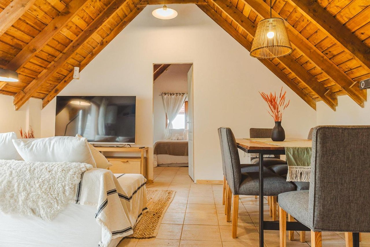 Hotel suite living area with a white sofa, dining table, and vaulted timber ceiling.
