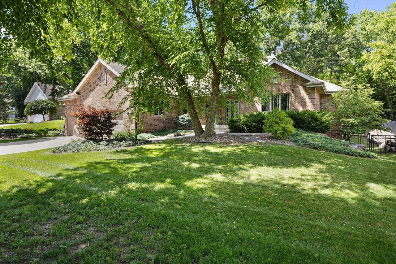 A large mature shade tree over a green lawn in front of a brick home in an established Madison neighborhood on a sunny day.