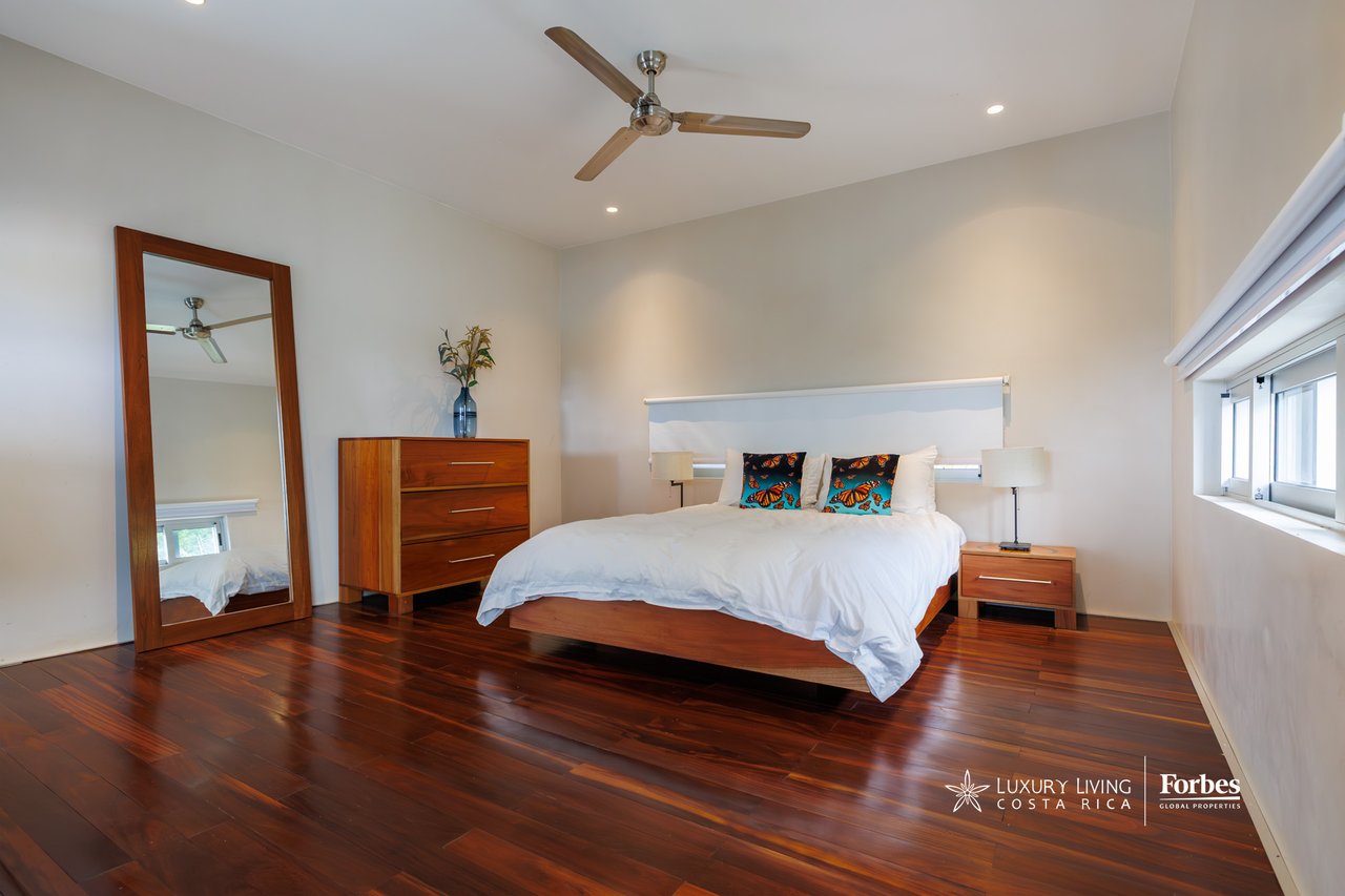 Bedroom with a white bed, butterfly-print pillows, polished wood floors, and a full-length mirror.