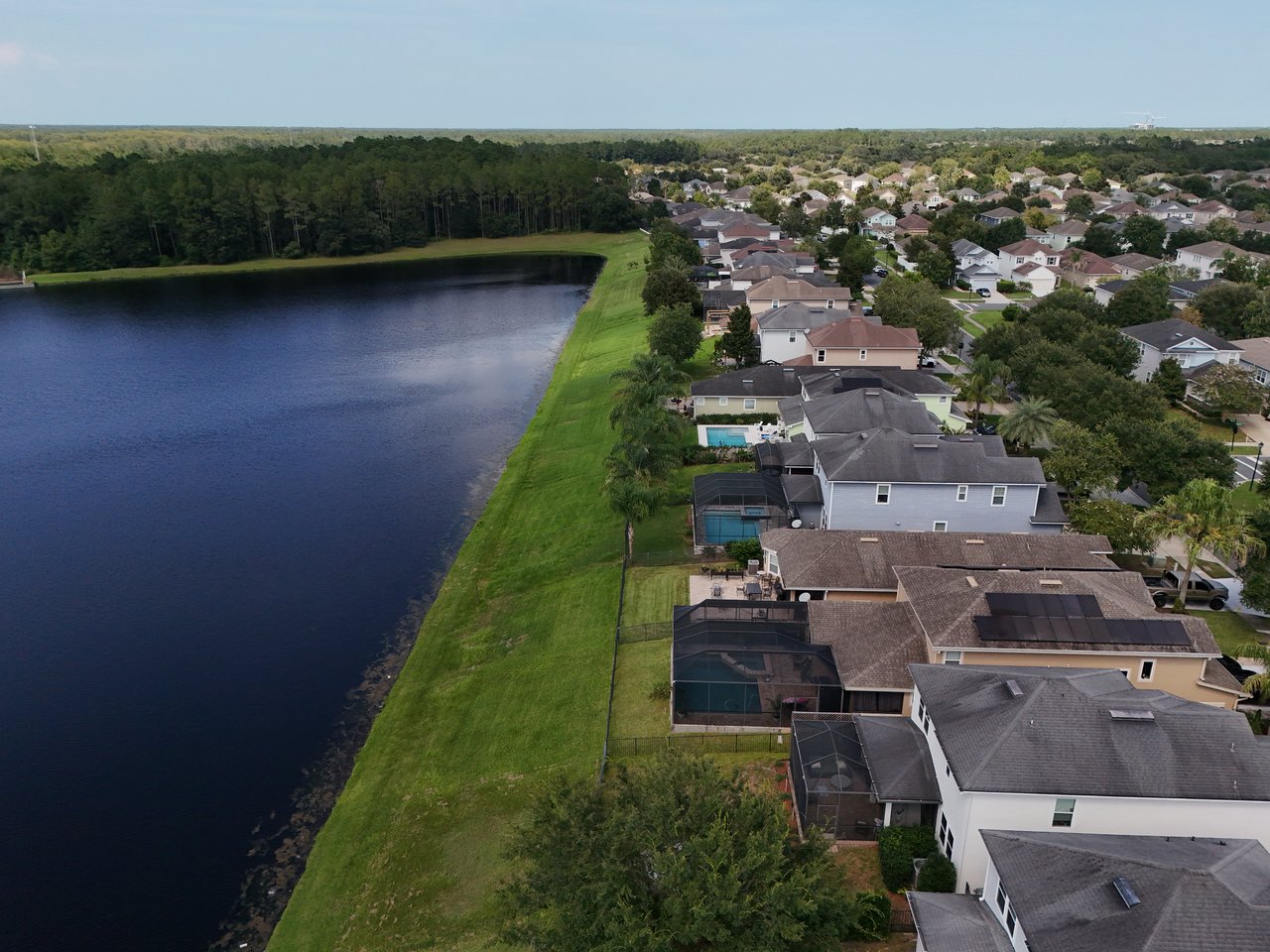 Aerial view of Greenleaf Village homes beside a pond, with screened pools and woods beyond.