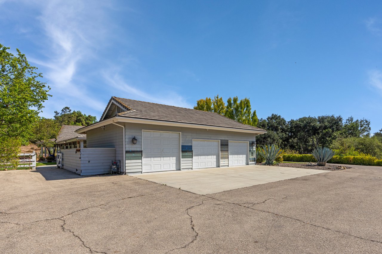 Gray three-bay garage with white paneled doors and a broad paved driveway.