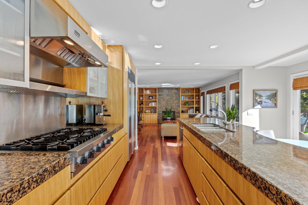 Open kitchen with wood cabinetry, granite counters, a large gas range, and a long island with double sink.