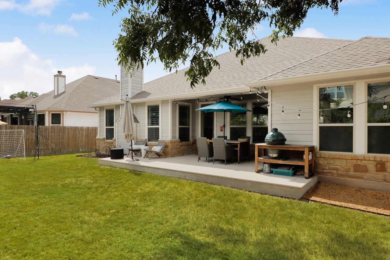 Backyard with a broad lawn and furnished patio, outdoor dining area, ceramic grill, and string lights.