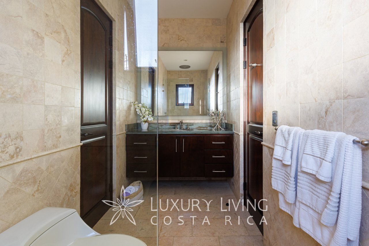 Bathroom with beige stone tile, dark wood vanity, glass shower partition, and white towels.