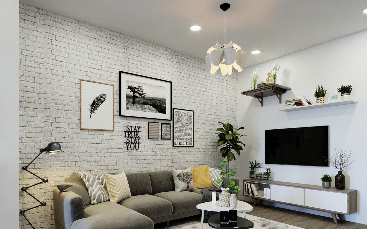Living room with a gray sectional, white brick accent wall, framed art, and wall-mounted television.