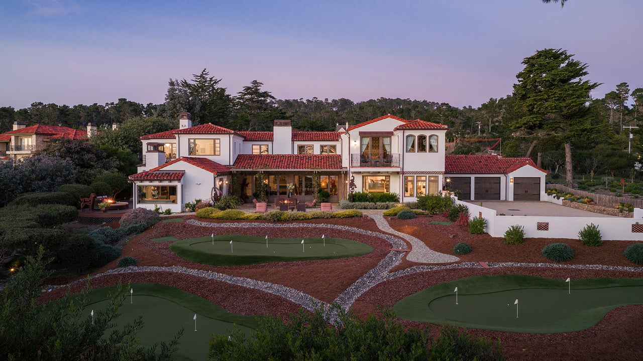 Mediterranean-style home with red tile roofs and landscaped putting greens at dusk.