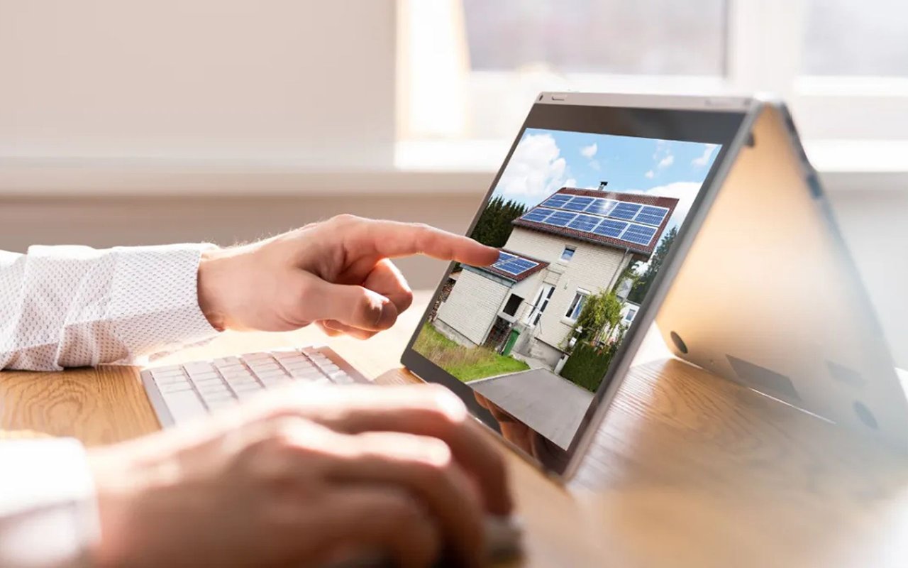 A person points to a solar-panel-equipped house in a listing displayed on a tablet.