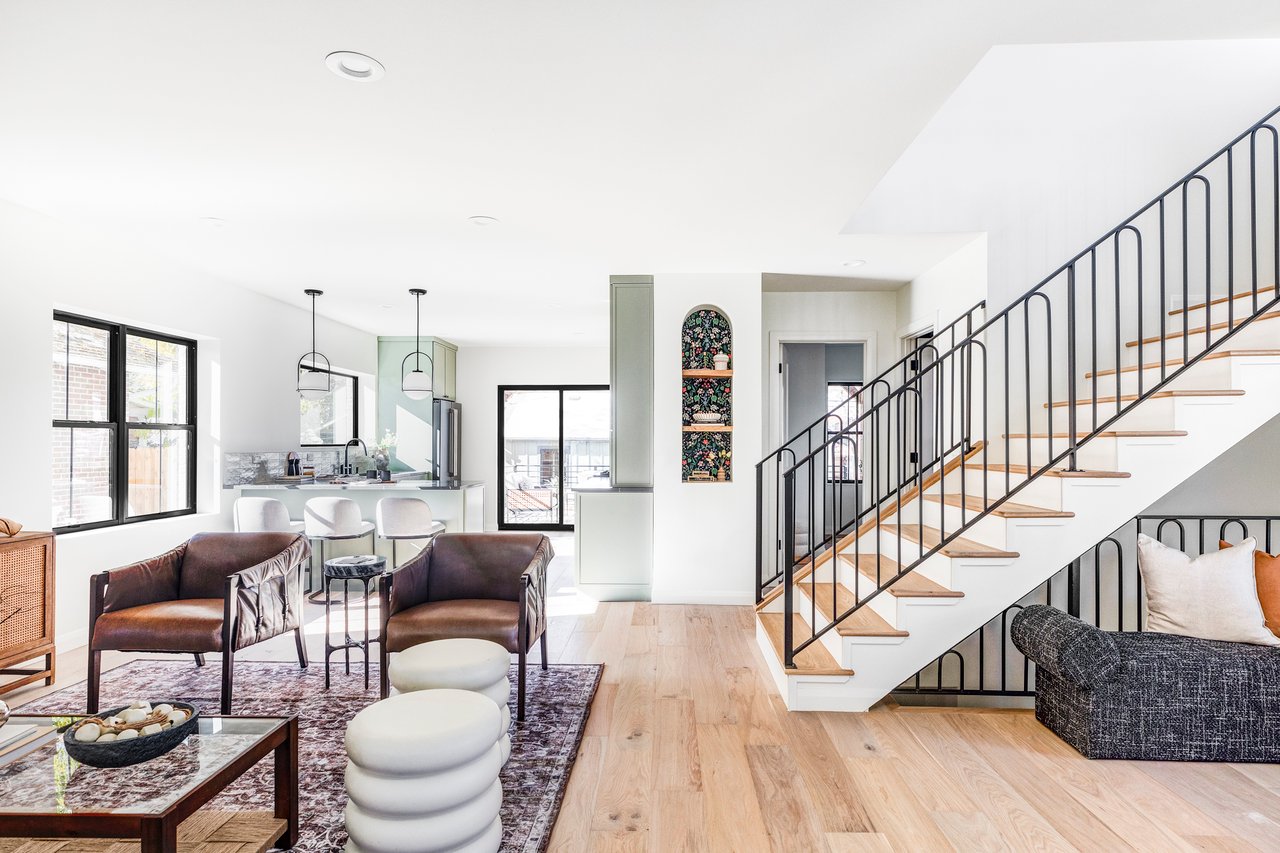 Open-concept living room and kitchen with black metal staircase, hardwood floors, and modern furnishings