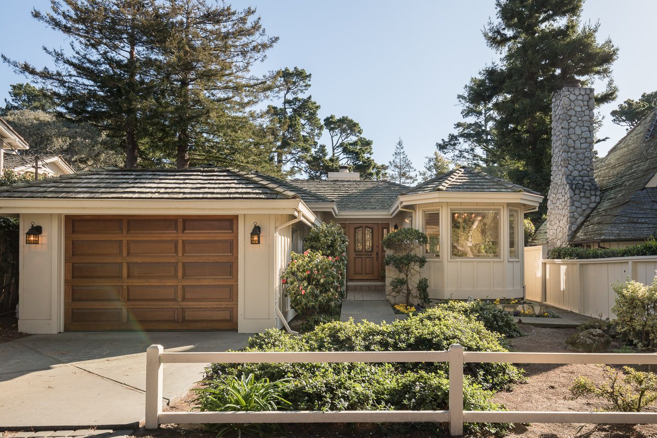 Single-story home with a wooden garage door, stone chimney, and landscaped front garden.