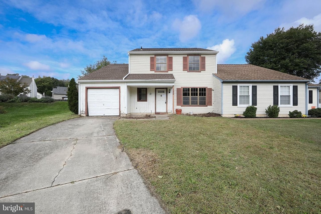 Light-colored house with an attached garage, long driveway, and broad front lawn.
