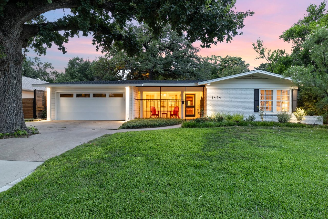 Twilight front elevation of the mid-century modern brick home at 2404 Westover Rd, Tarrytown, beneath mature oak trees.