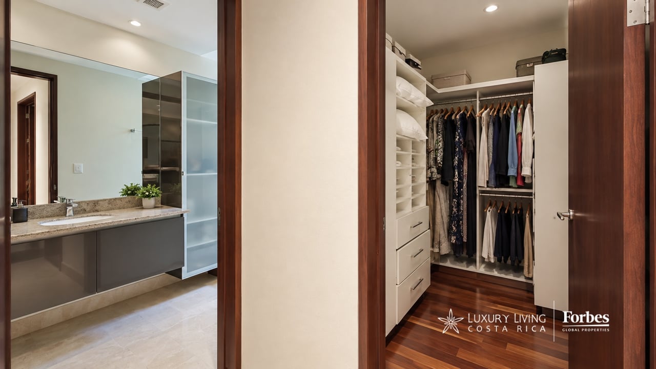Bathroom vanity beside a walk-in closet with organized clothing and wood flooring.