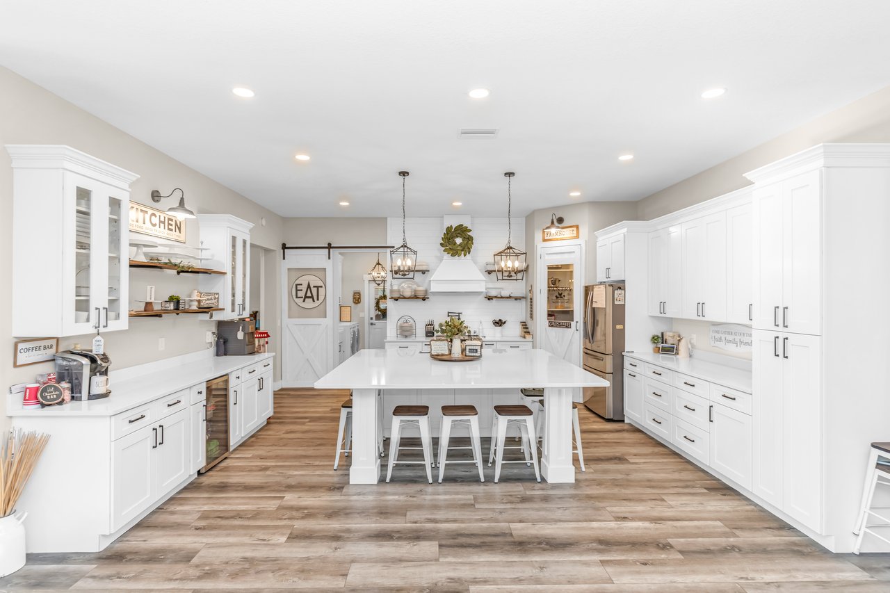 Farmhouse kitchen with a large white island, three stools, extensive cabinetry, and wood-look flooring.