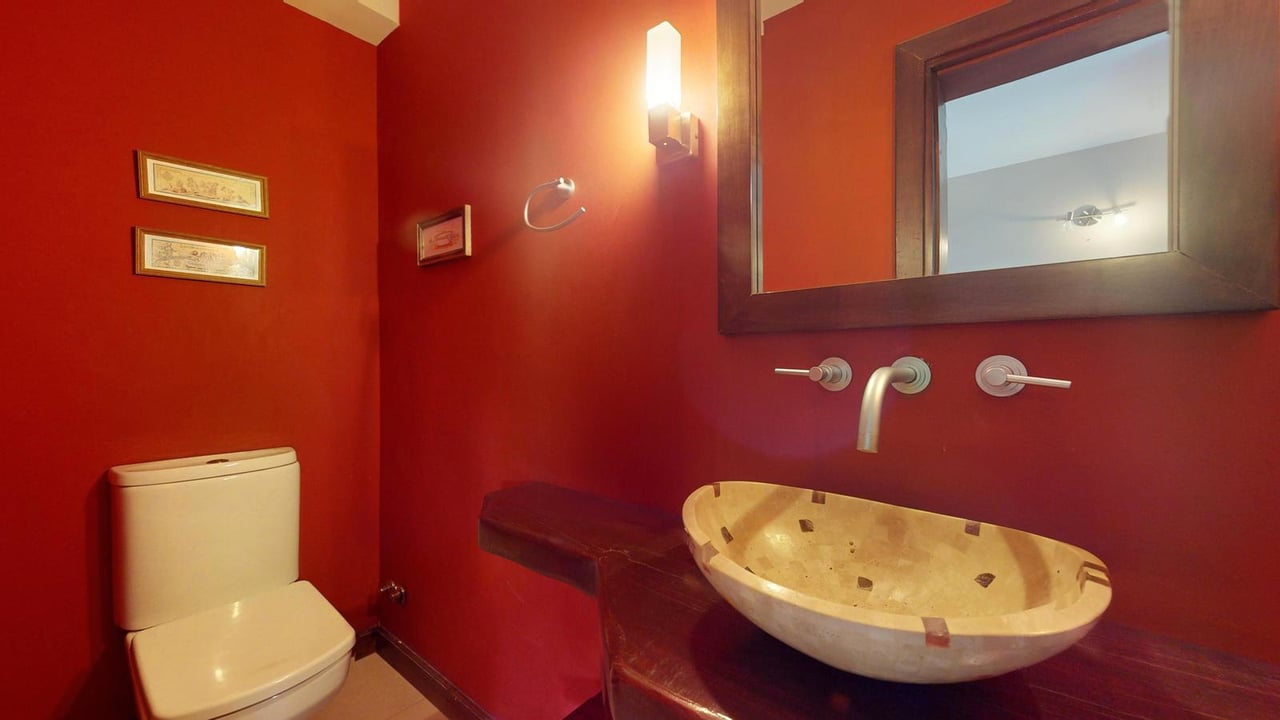 Red bathroom with a cream vessel sink, dark stone counter, and white toilet.