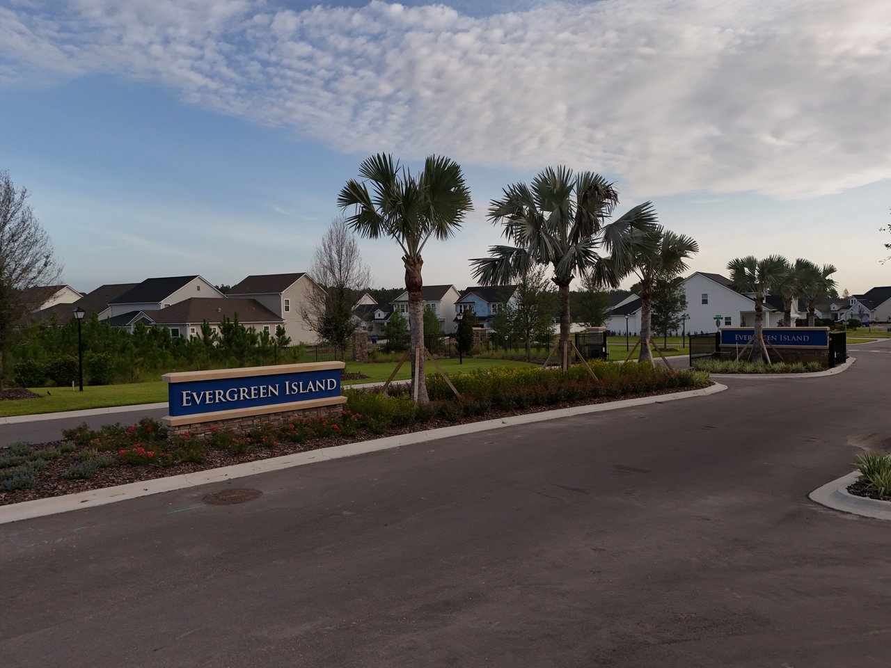 Evergreen Island neighborhood entrance with blue signs, palm trees, and homes along the road.