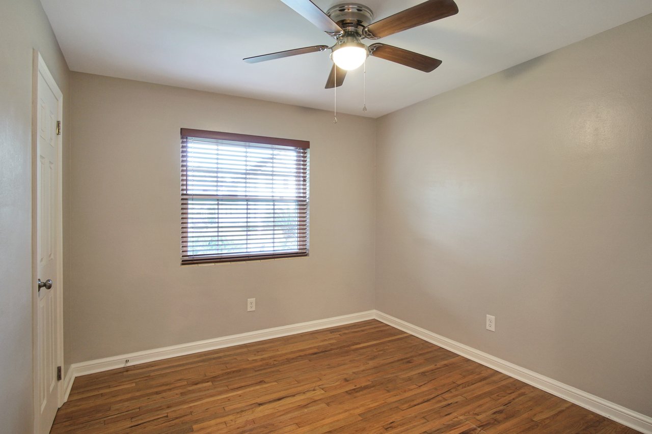 An empty utility room featuring hardwood floors and a ceiling fan, creating a spacious and airy atmosphere.