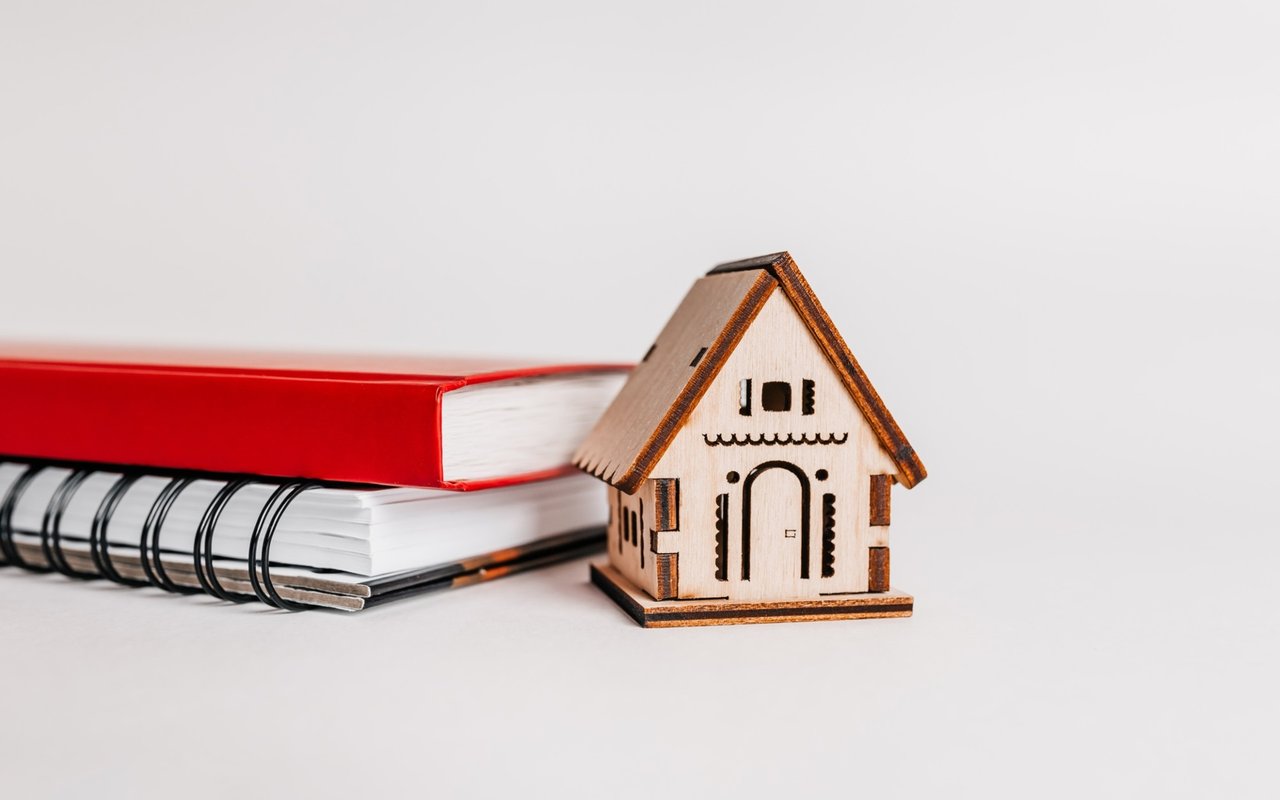 Wooden model house beside a stack of notebooks.