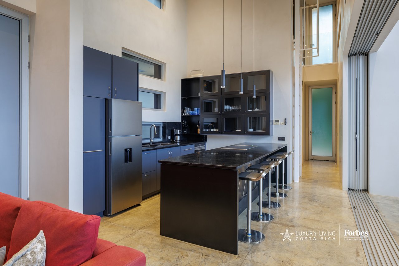 Modern kitchen with a black stone island, bar stools, and dark blue cabinetry.