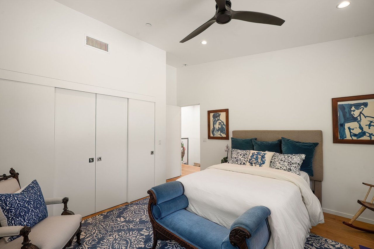 Bedroom with a white bed, blue accents, patterned rug, and ceiling fan.