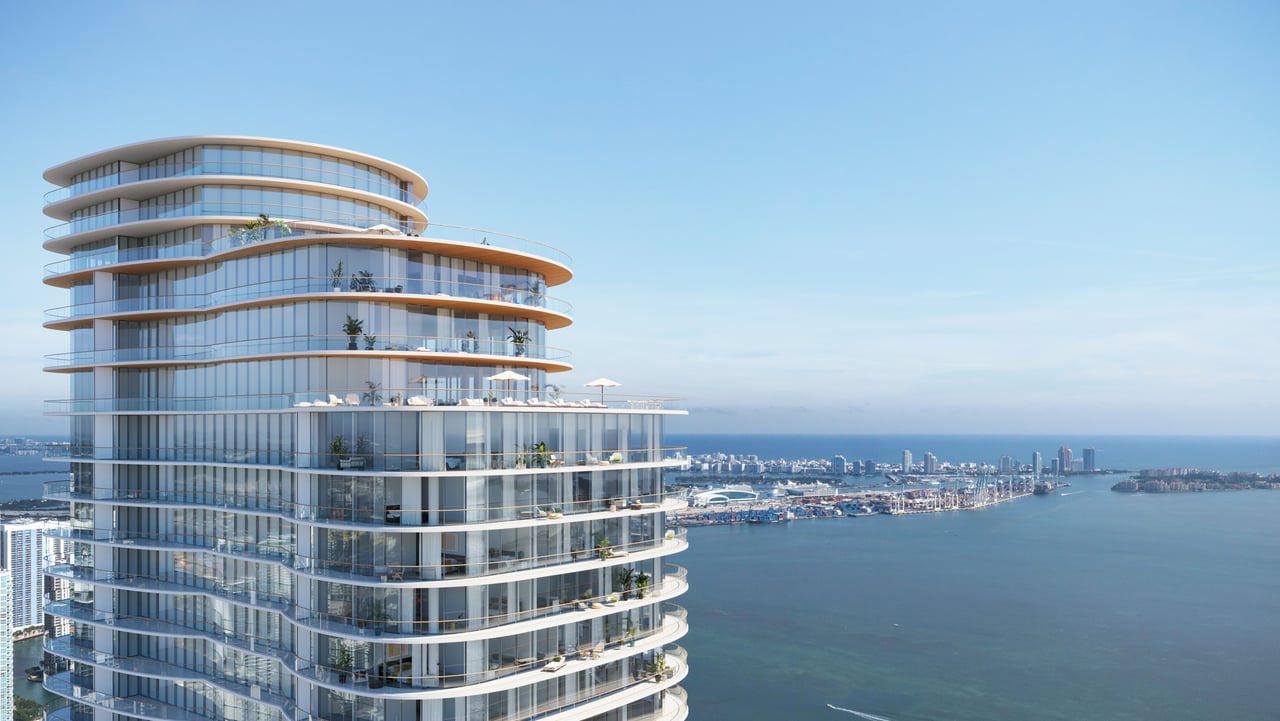 Curved glass residential tower overlooking Biscayne Bay and the Miami skyline.