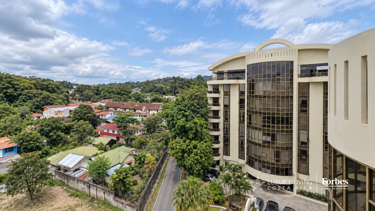 Modern cream-colored apartment building with a curved glass facade beside a leafy residential neighborhood.