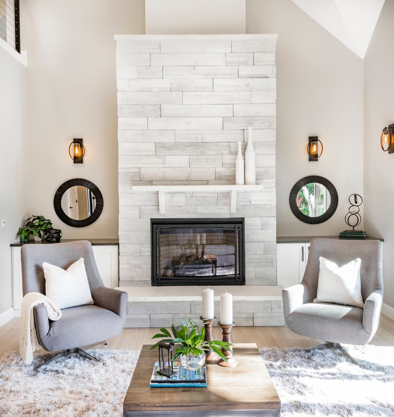 Living room with a whitewashed stone fireplace, gray armchairs, and a wood coffee table.