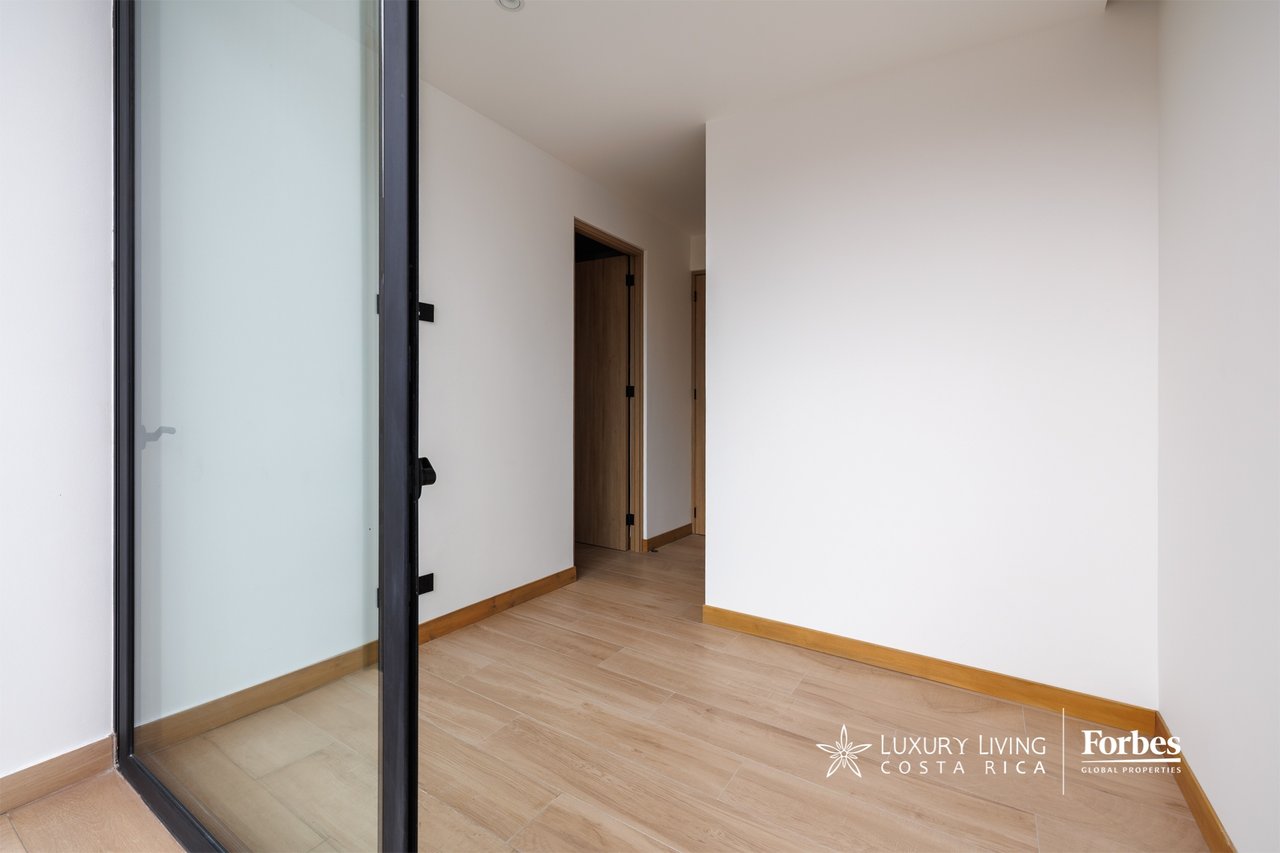 Empty hallway with light wood-look flooring, wooden trim, and a black-framed glass door.