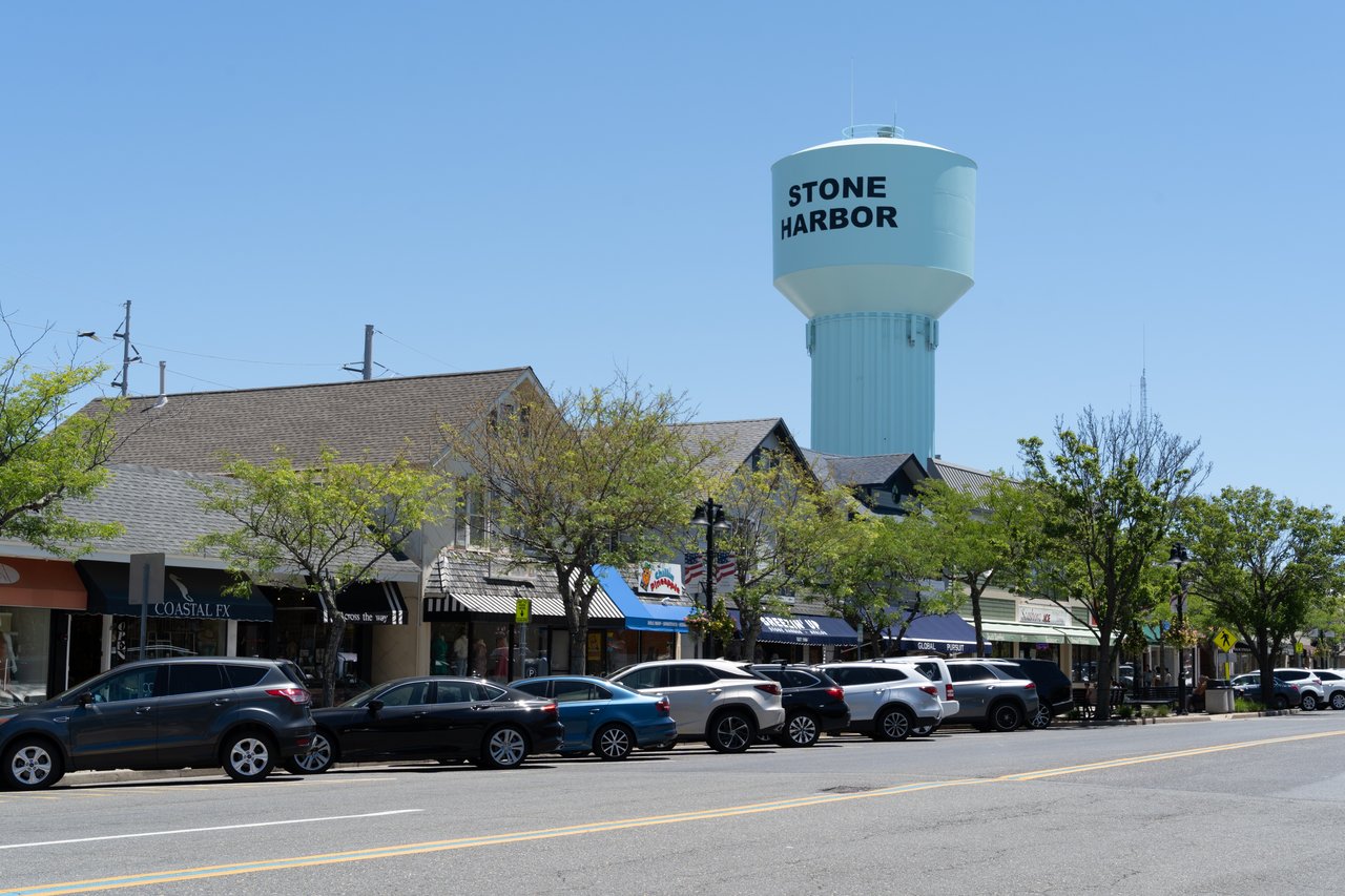 Stone Harbor water tower above a tree-lined shopping street with parked cars.