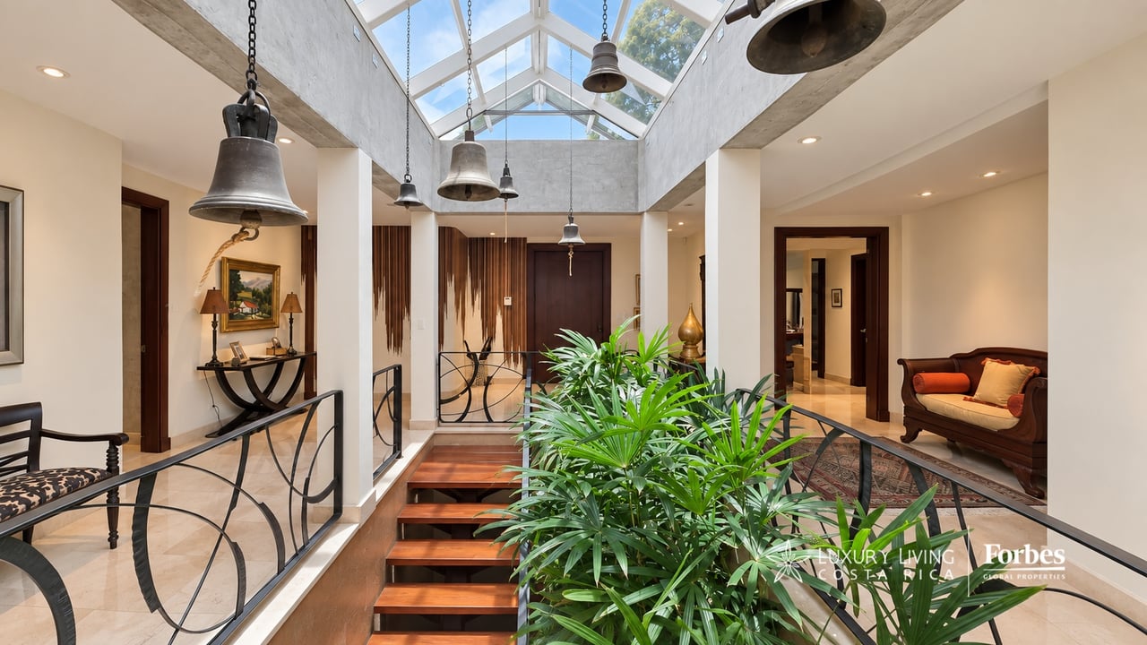 Foyer with a glass skylight, central indoor plants, and polished wood stairs.