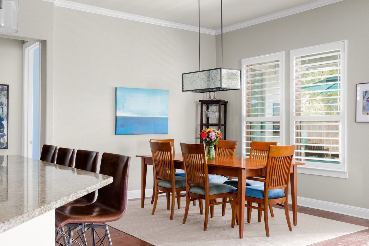 Dining room with a wooden table, blue-cushioned chairs, and white plantation shutters.