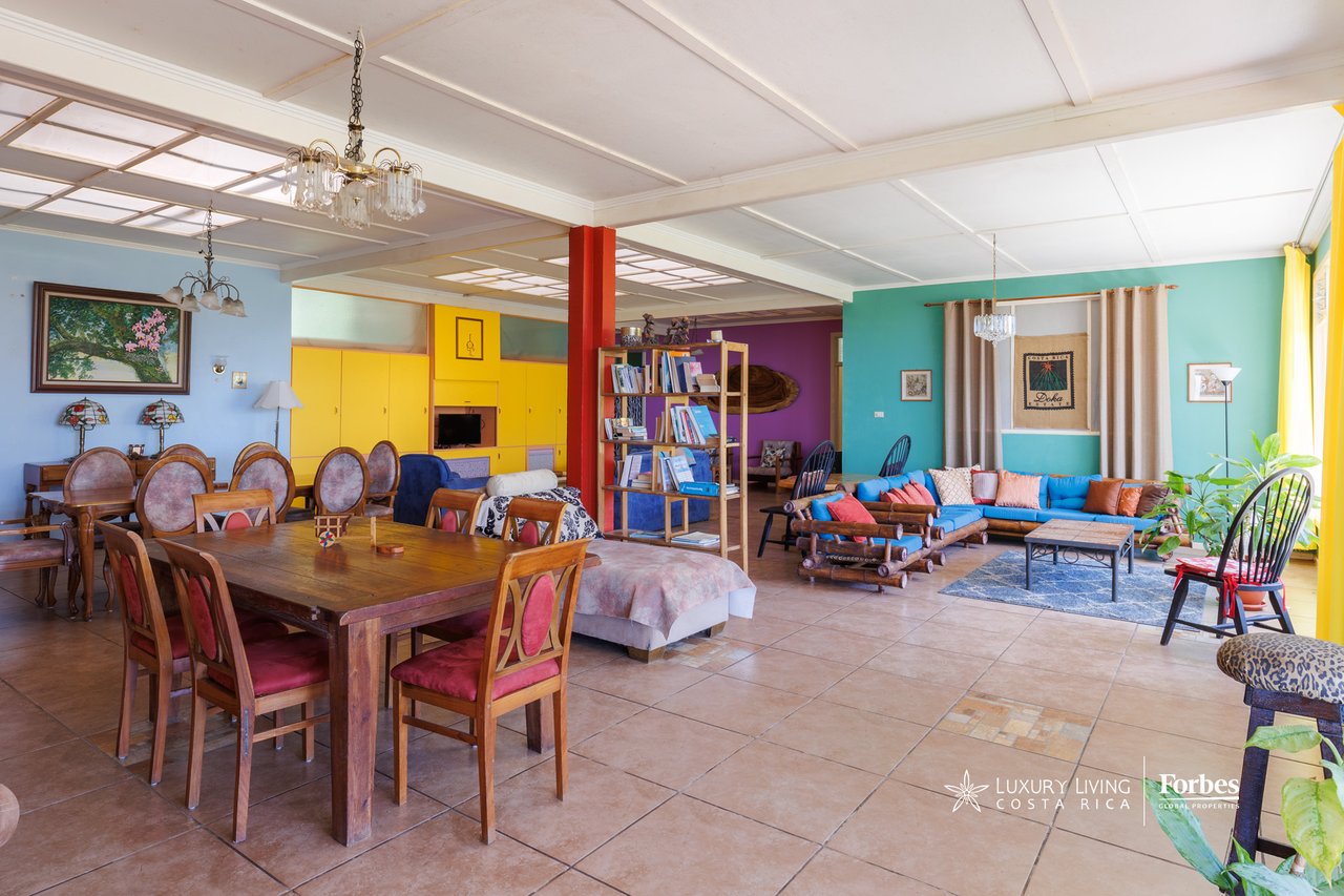 Open-plan living and dining room with colorful seating, a large wooden table, and turquoise and yellow walls.