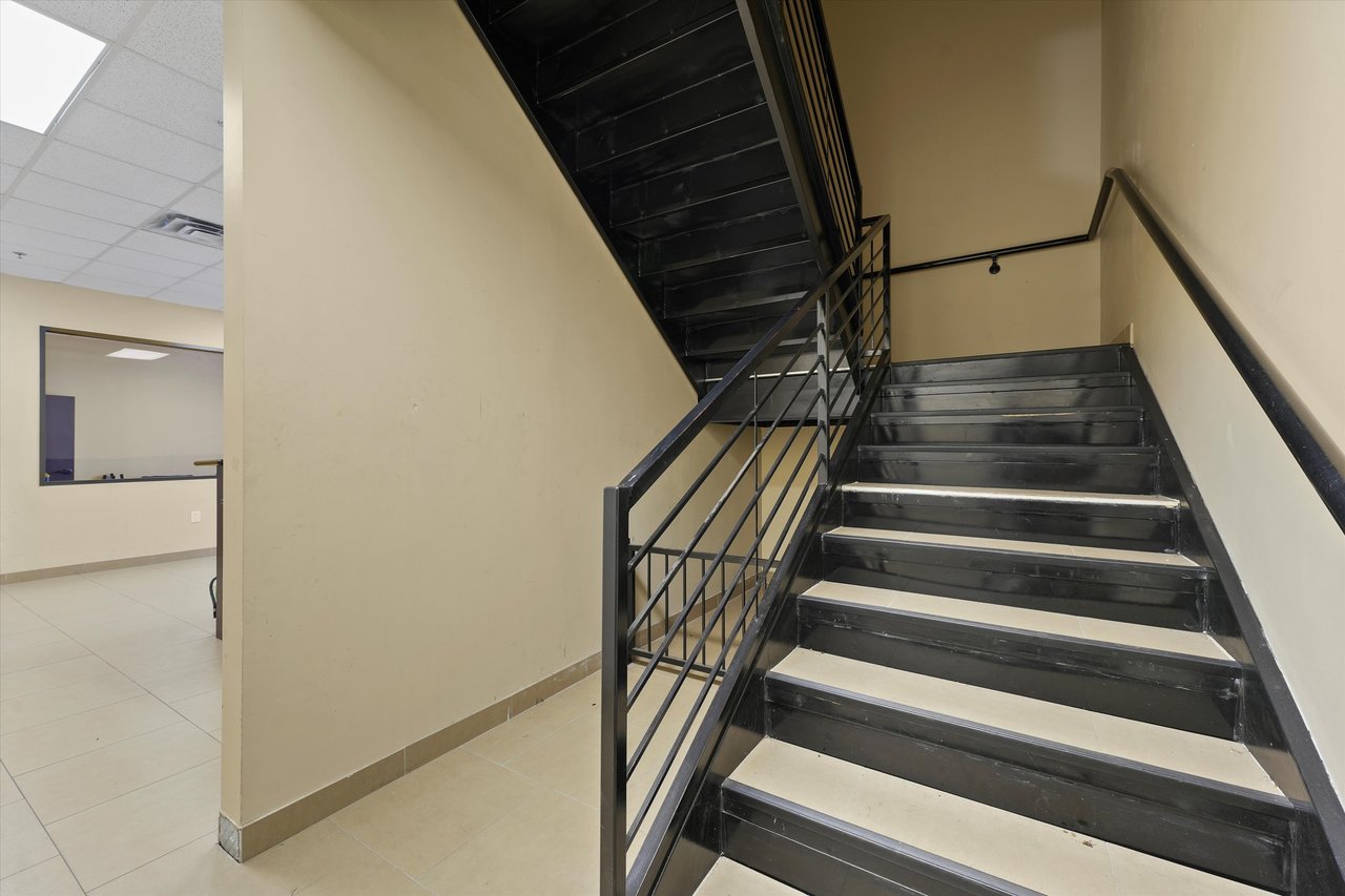 Commercial interior staircase with black metal railings and tiled steps beside an office area.